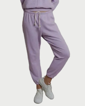 Person wearing a lavender tracksuit with white sneakers on a plain background