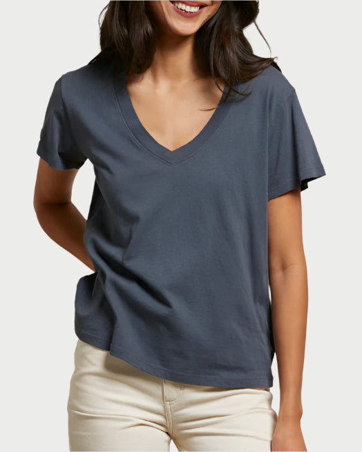 A woman wearing the perfectwhitetee Hendrix V-Neck T-Shirt in Night and light-colored pants stands smiling with one hand behind her back against a plain background.