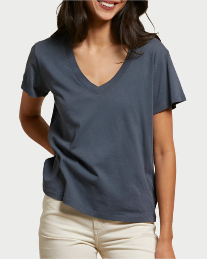 A woman wearing the perfectwhitetee Hendrix V-Neck T-Shirt in Night and light-colored pants stands smiling with one hand behind her back against a plain background.