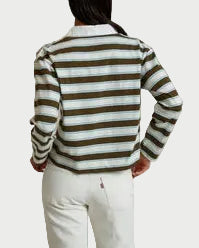 Person wearing a striped sweater and white pants standing against a beige backdrop