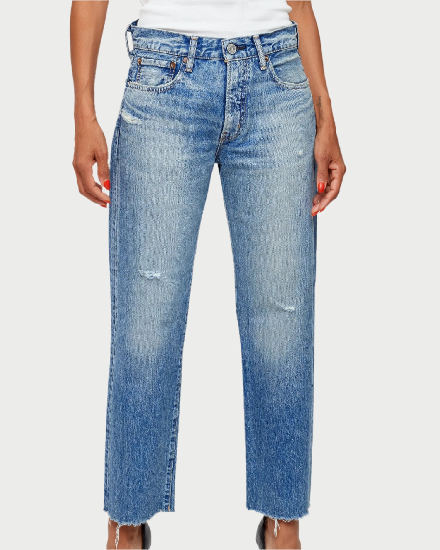 A person wears Moussy Kossuth Boy Jeans—high-waisted, heavyweight, straight-leg denim in a light blue wash with slight knee distressing and raw hems—paired with a white top. Only the lower torso and legs are shown.