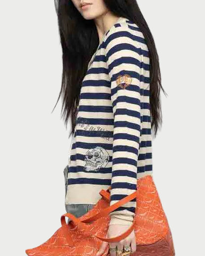 A woman with long dark hair wears the Zadig & Voltaire Missya Stripe Sweater with navy and white stripes and patches, holding an orange patterned tote bag against a plain light gray background.