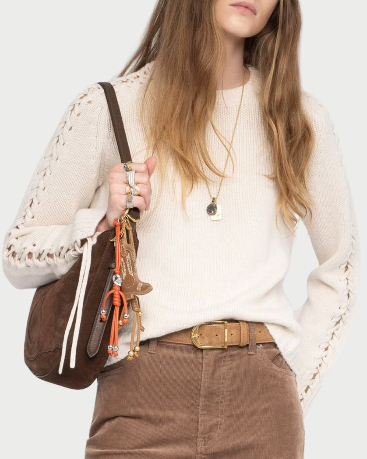 Woman wearing an ivory laced sleeve sweater holding a brown handbag against a white background