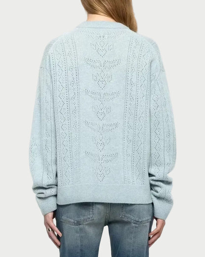A woman viewed from the back wearing a light blue cable-knit sweater and blue jeans against a plain light gray studio background.