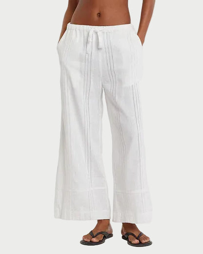 Woman wearing a striped tank top and white pants on a plain background