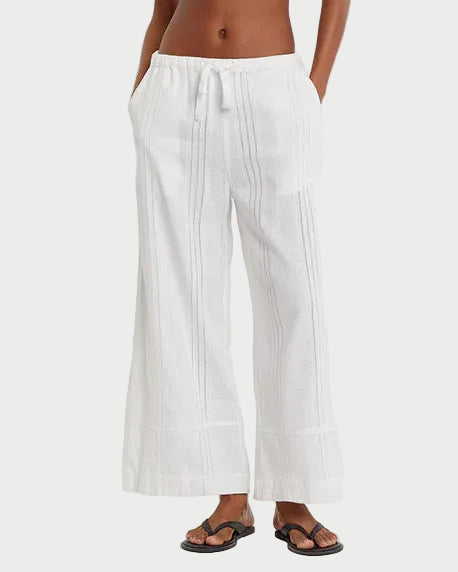 Woman wearing a striped tank top and white pants on a plain background