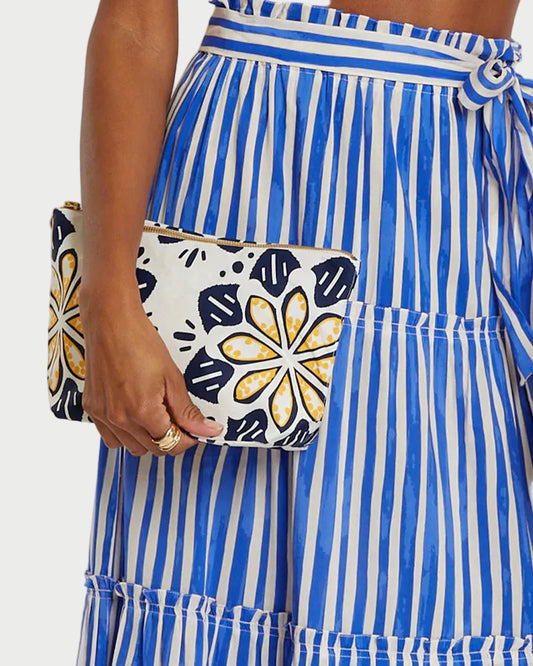 Person wearing a blue and white striped dress holding a floral clutch against a plain background
