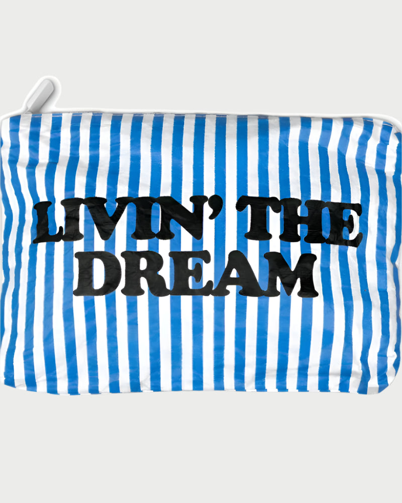 Introducing the Printed Pouch - Livin' The Dream by LOCAL BEACH: a travel toiletries organizer with a sleek design featuring blue and white vertical stripes, a top zipper, and made from water-resistant Tyvek fabric. It prominently displays the bold phrase "LIVIN' THE DREAM" across the front.