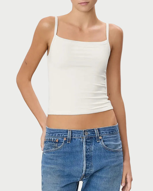 Woman wearing a white tank top and blue jeans on a light gray background