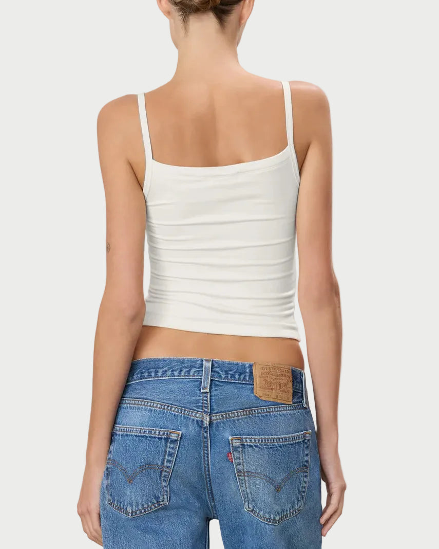 Person wearing a white tank top and blue jeans on a plain background