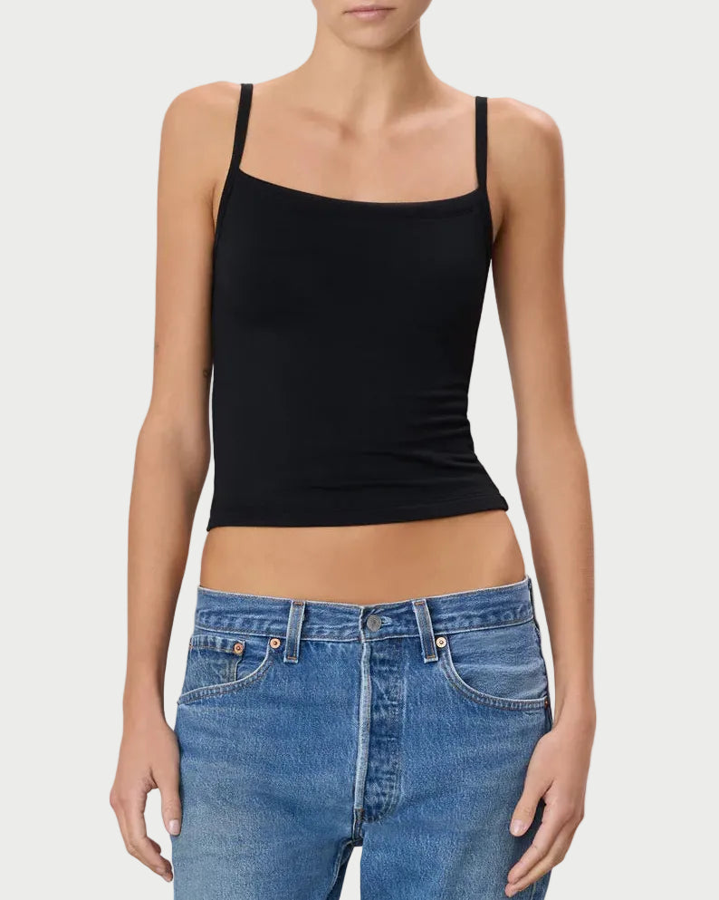 Woman wearing a black tank top and blue jeans against a plain background