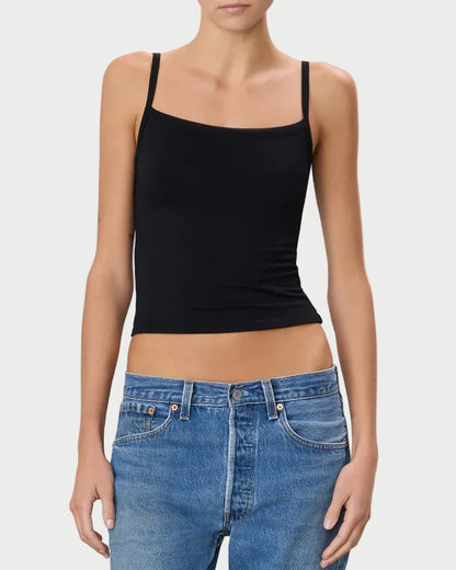 Woman wearing a black tank top and blue jeans against a plain background