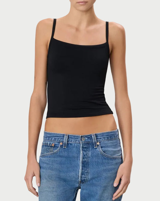 Woman wearing a black tank top and blue jeans against a plain background