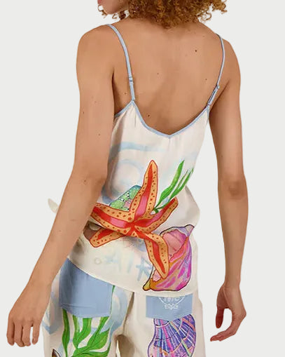 A person with curly hair, facing away from the camera, wears a light Me369 Angelique Camisole and pants—the outfit features ME369's colorful ocean-inspired prints such as starfish and seashells.