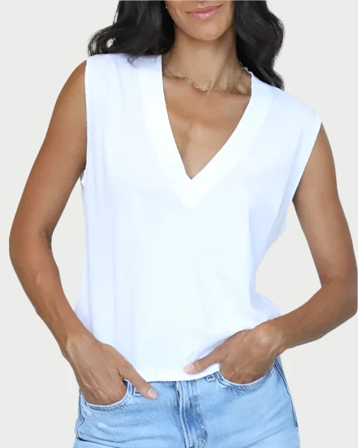 A person wearing a Margot V Neck Sleeveless Tee by perfectwhitetee and light blue jeans is standing against a plain background, their hands casually tucked in their pockets.