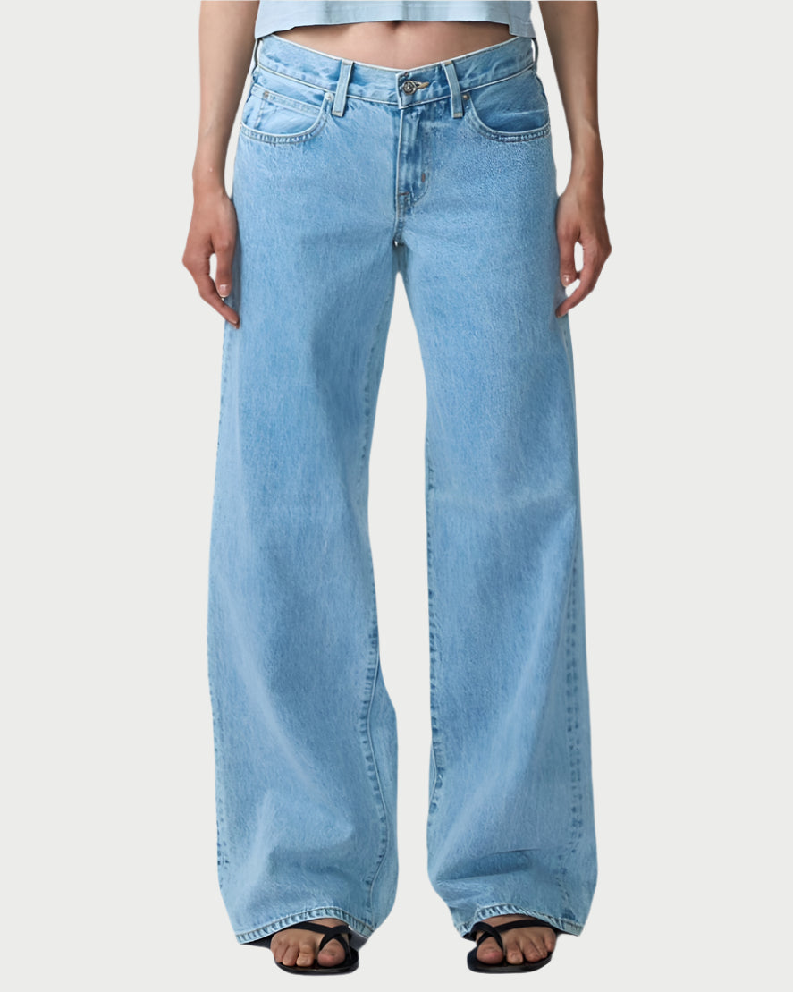 A person wears a light blue crop top and SLVRLAKE's Mica Jeans in Clear Skies, made from regenerative cotton. The high-waisted, wide-leg jeans offer a vintage look, elegantly touching the ground and paired with chic black heels.