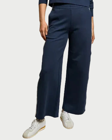 Only the lower half of a person is visible, showing them in perfectwhitetee Mikos Wide Leg Pant—a high waisted, premium cotton navy blue style—paired with white sneakers against a plain background.