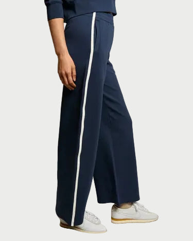 A person models the perfectwhitetee Mikos Wide Leg Pant by perfectwhitetee—high waisted, navy, with a white side stripe—paired with white socks and sneakers, standing against a plain light background.