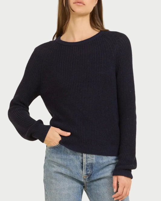 Woman wearing a navy sweater and blue jeans against a beige background
