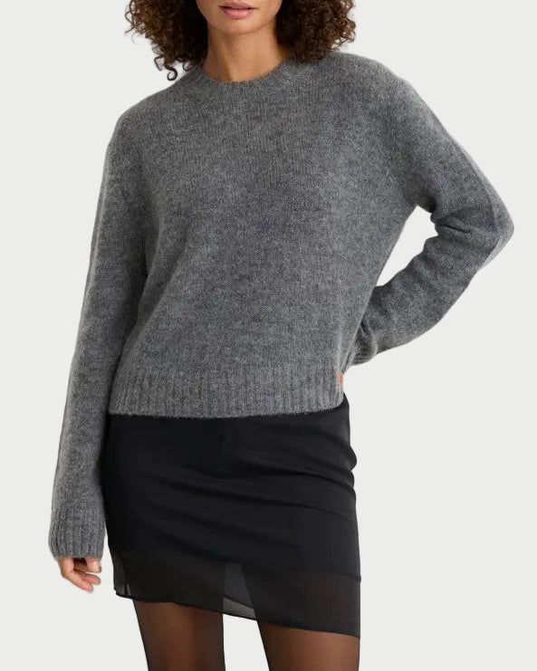 A person wears a grey One Grey Day Levanzo Pullover, a merino wool crew-neck sweater with long sleeves, a ribbed hem, and a refined silhouette.