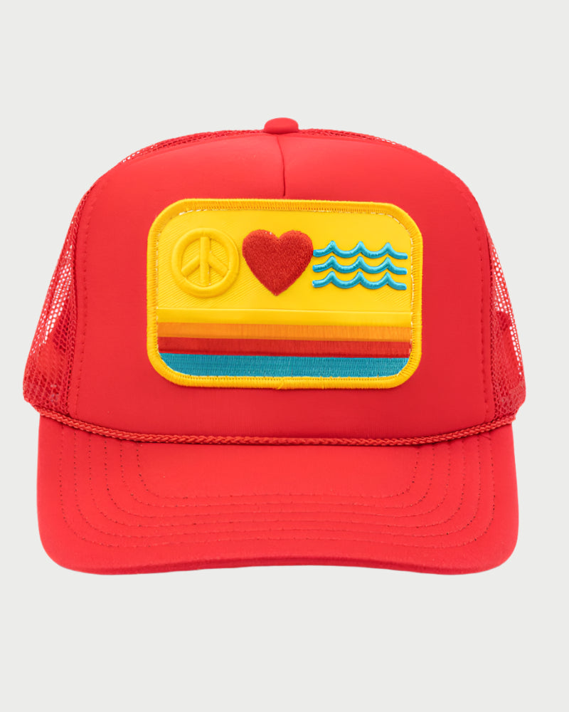 The Peace Love Waves Trucker Hat by LOCAL BEACH is a red cap featuring a mesh back and an embroidered patch with a peace sign, heart, and waves on vibrant yellow, orange, and blue stripes on a cheerful yellow background.
