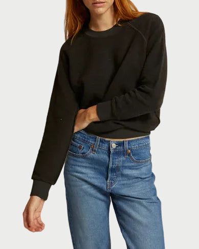 Woman wearing a black sweater and blue jeans against a beige background