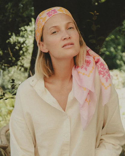 Woman in a cream outfit with a colorful headscarf sitting outdoors.