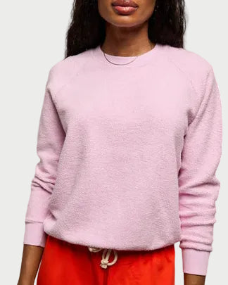 Woman wearing a light pink sweater and red pants against a plain background