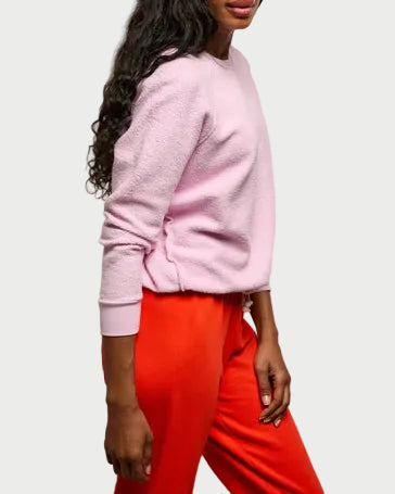 Woman wearing a pink sweater and red pants against a plain background