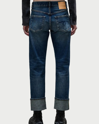 A person is shown from the back wearing R13 Cuffed Romeo Caslon Selvedge Blue jeans in a slim boyfriend fit with visible stitching, logo back pockets, a tan waistband patch, and black boots.