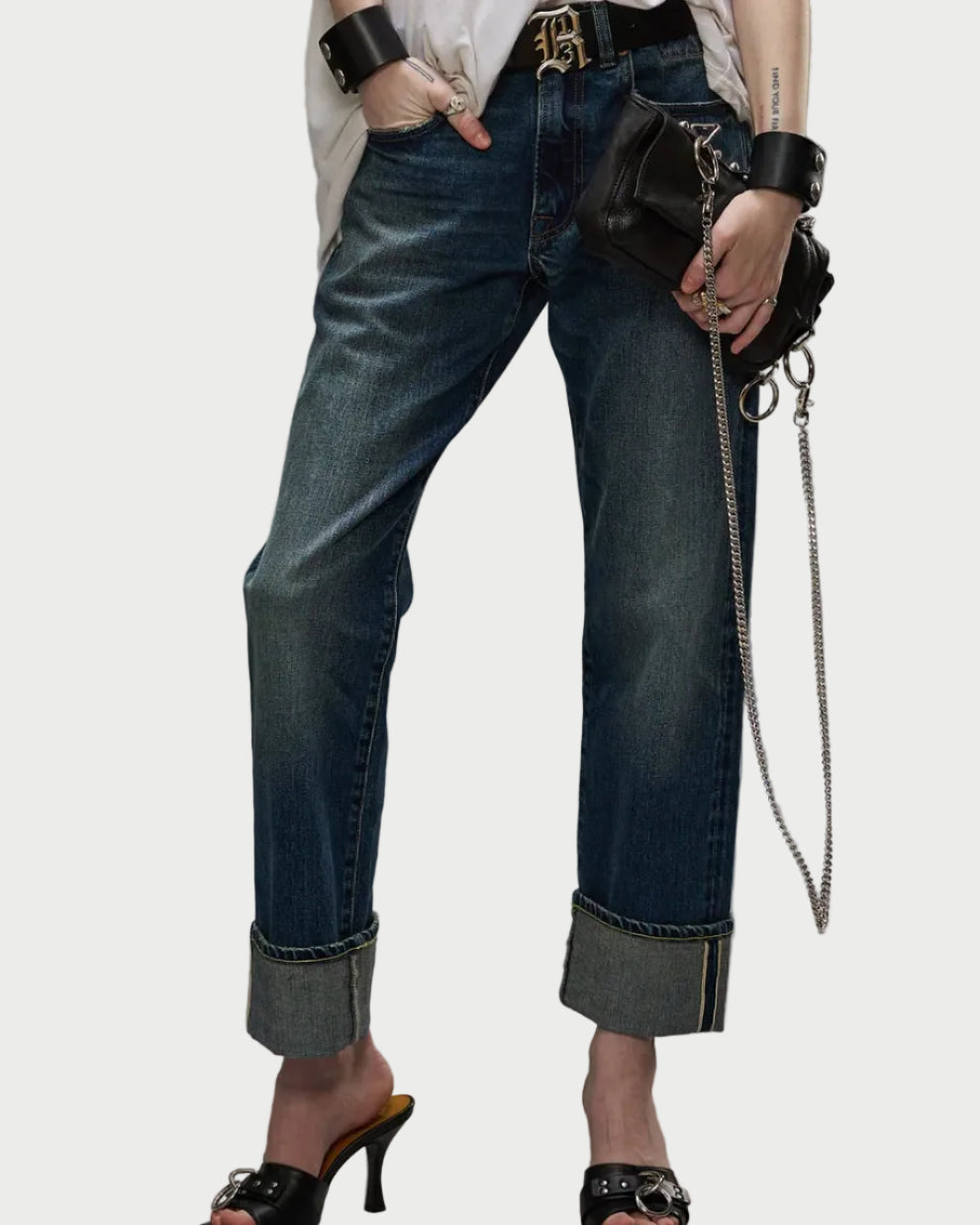 Wearing R13 Cuffed Romeo Caslon Selvedge Blue jeans in a slim boyfriend fit with black high-heeled sandals, a white top, chunky bracelets, rings, and a black leather chain-strap handbag.