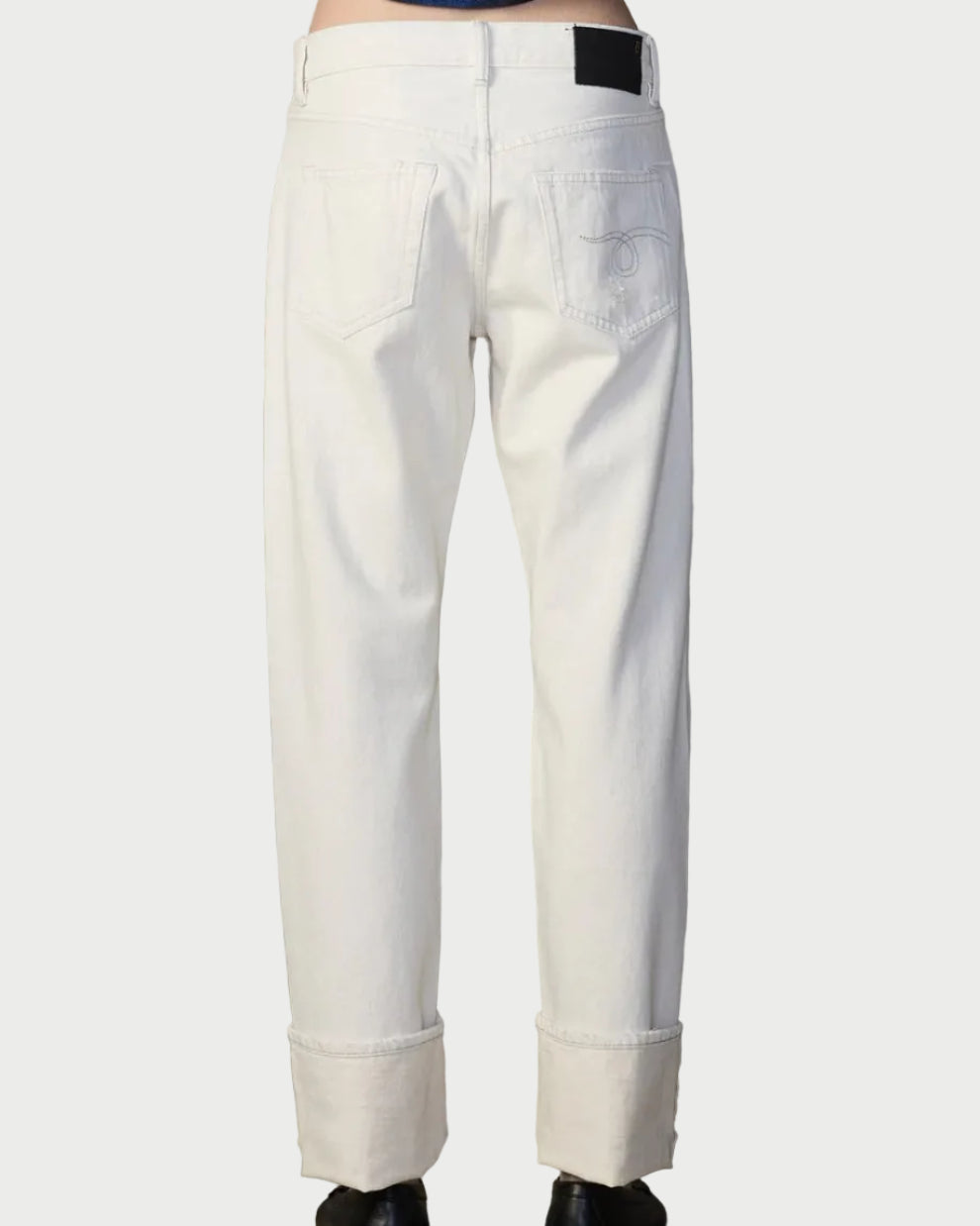 Person wearing white pants and a blue patterned top against a textured wall.