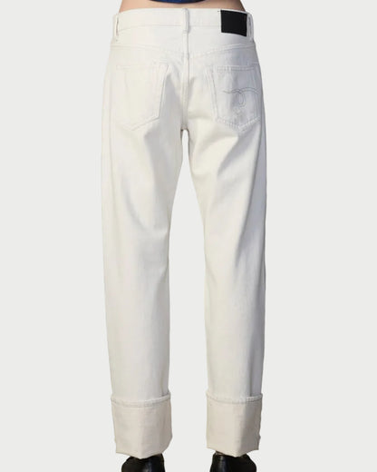 Person wearing white pants and a blue patterned top against a textured wall.