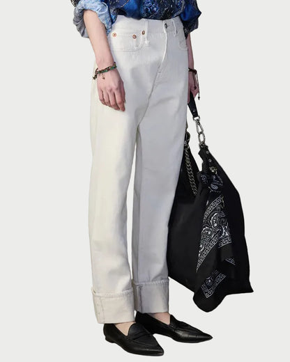 Person wearing a blue patterned shirt, white pants, and black shoes against a textured wall.