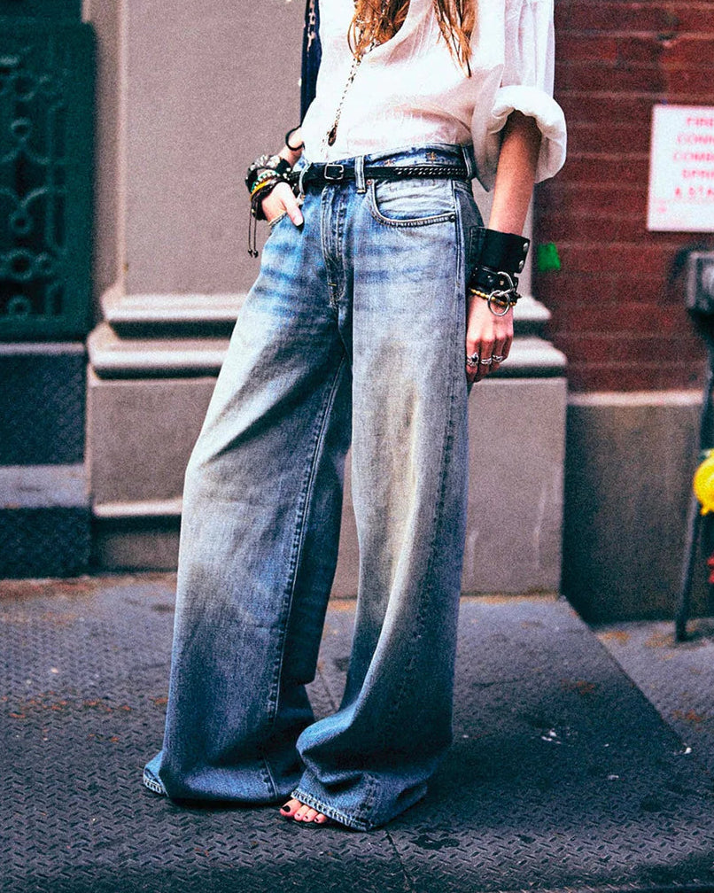 Person wearing a white shirt, blue jeans, and a bandana on a city street.