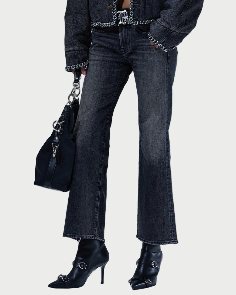 Person wearing a black denim jacket and jeans with a black handbag against a light gray background