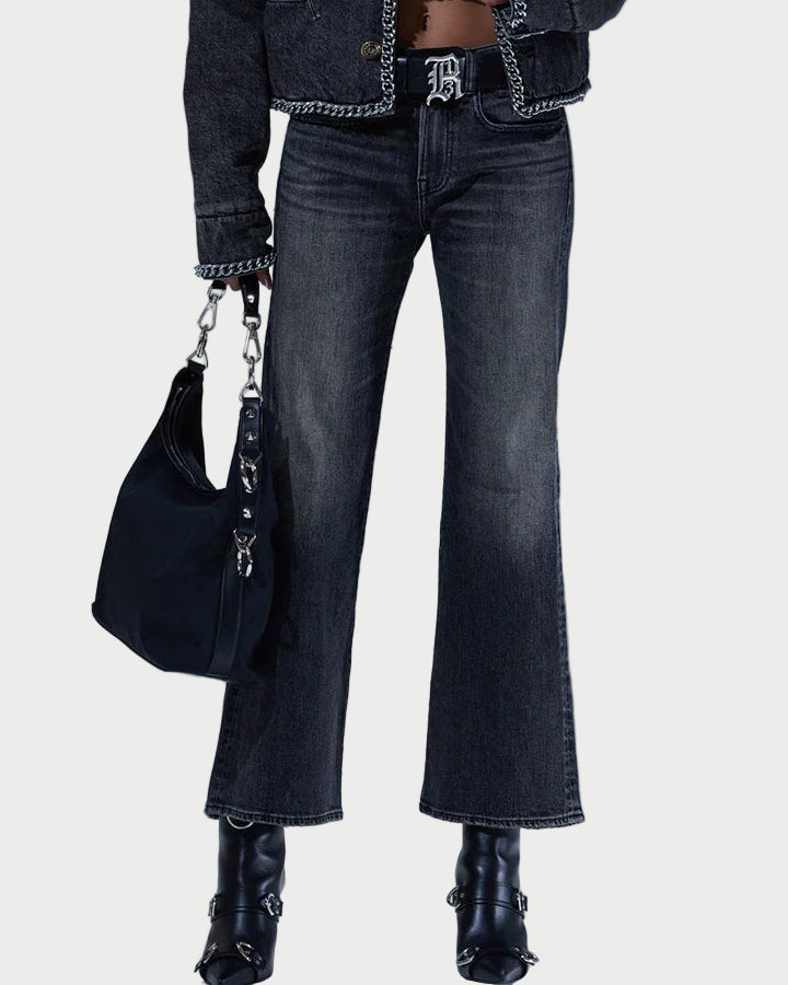 Woman wearing a dark denim jacket, jeans, and black boots with a black handbag against a light gray background.