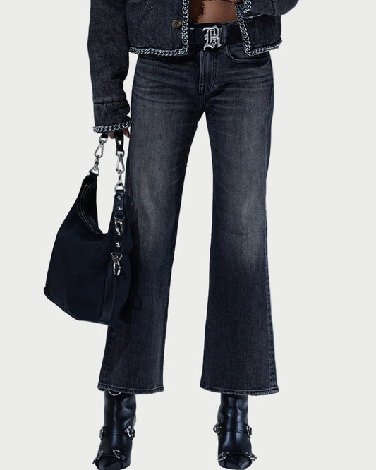 Woman wearing a dark denim jacket, jeans, and black boots with a black handbag against a light gray background.