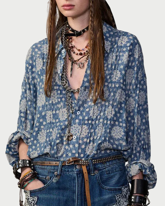 Woman wearing a blue floral blouse and denim shorts against a textured wall.