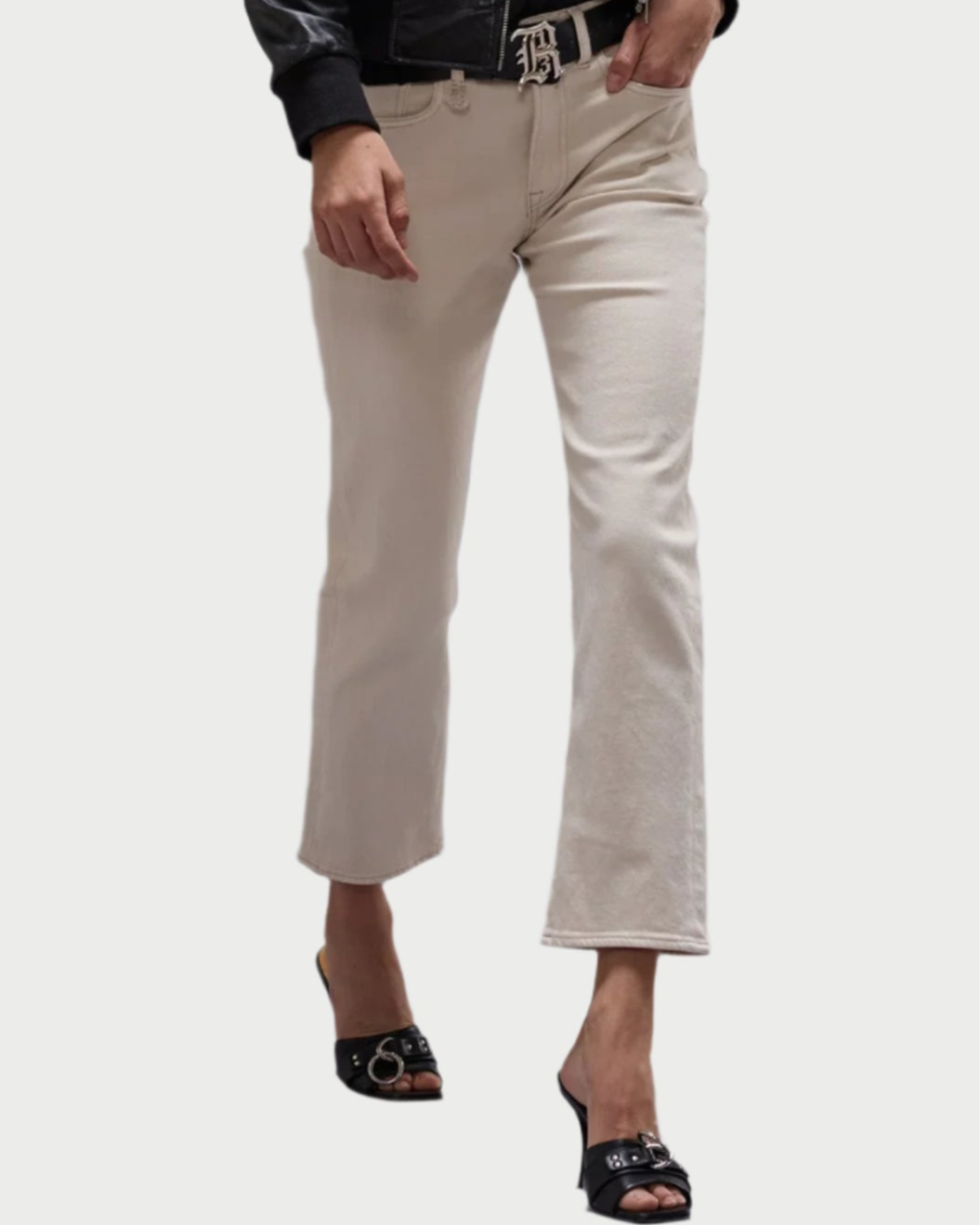 A person wears R13 Romeo Jean in Ecru, styled with a black belt, black jacket, and heeled sandals. The slim boyfriend jeans in Japanese comfort stretch denim are by R13, shown against a plain background.