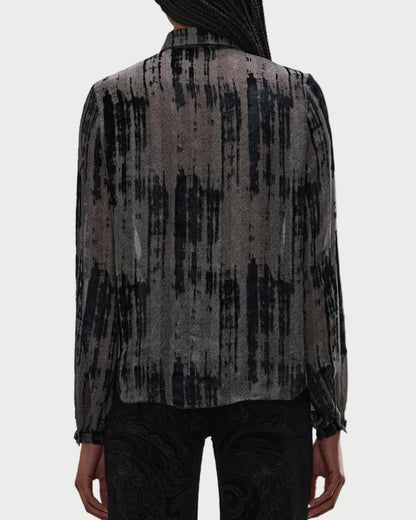 A person faces away, wearing the R13 Ruffle Blouse—a sheer grey top with a black abstract vertical pattern by R13. Only their upper body and part of the arms are visible.