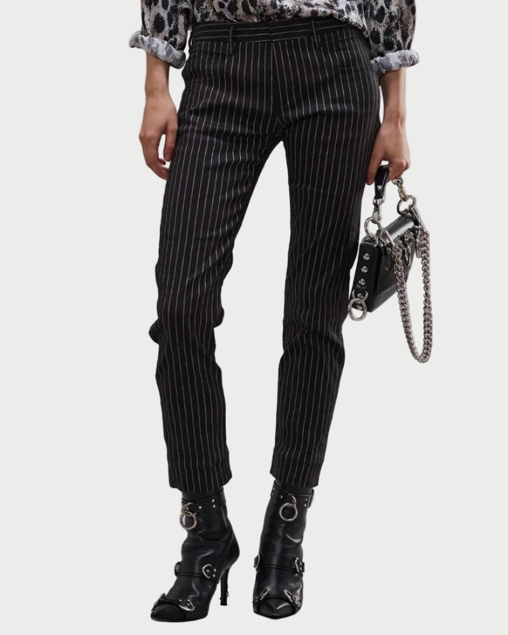 Wearing R13 Tailored Boy Straight Pants in black pinstripe, a patterned rolled-sleeve shirt, black heeled ankle boots with buckles, and carrying a small black handbag with a silver chain strap.