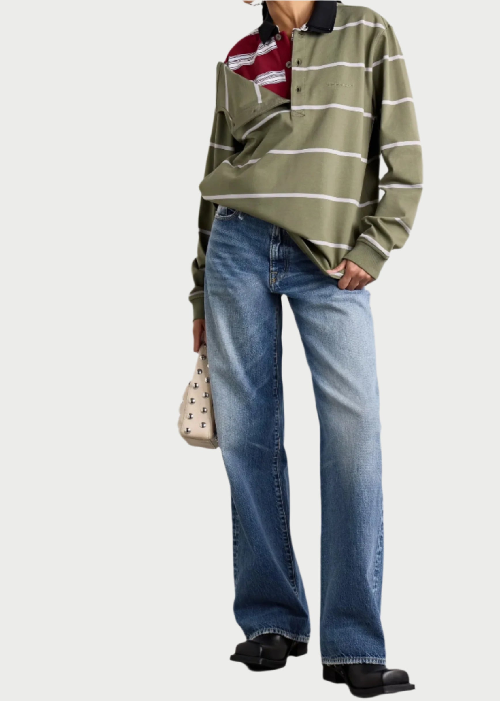 A person wears a green and burgundy striped long-sleeve polo shirt with R13 D'arcy Jeans, giving a vintage vibe. They finish the look with black shoes and a small beige handbag adorned with an "X" pattern.