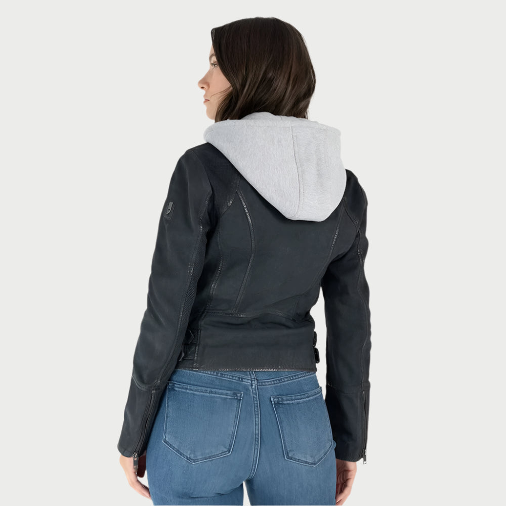 A person with long hair, facing away from the camera, wears a Mauritius Soft Nubuck Leather Jacket over a removable gray hoodie and blue jeans against a plain light backdrop.