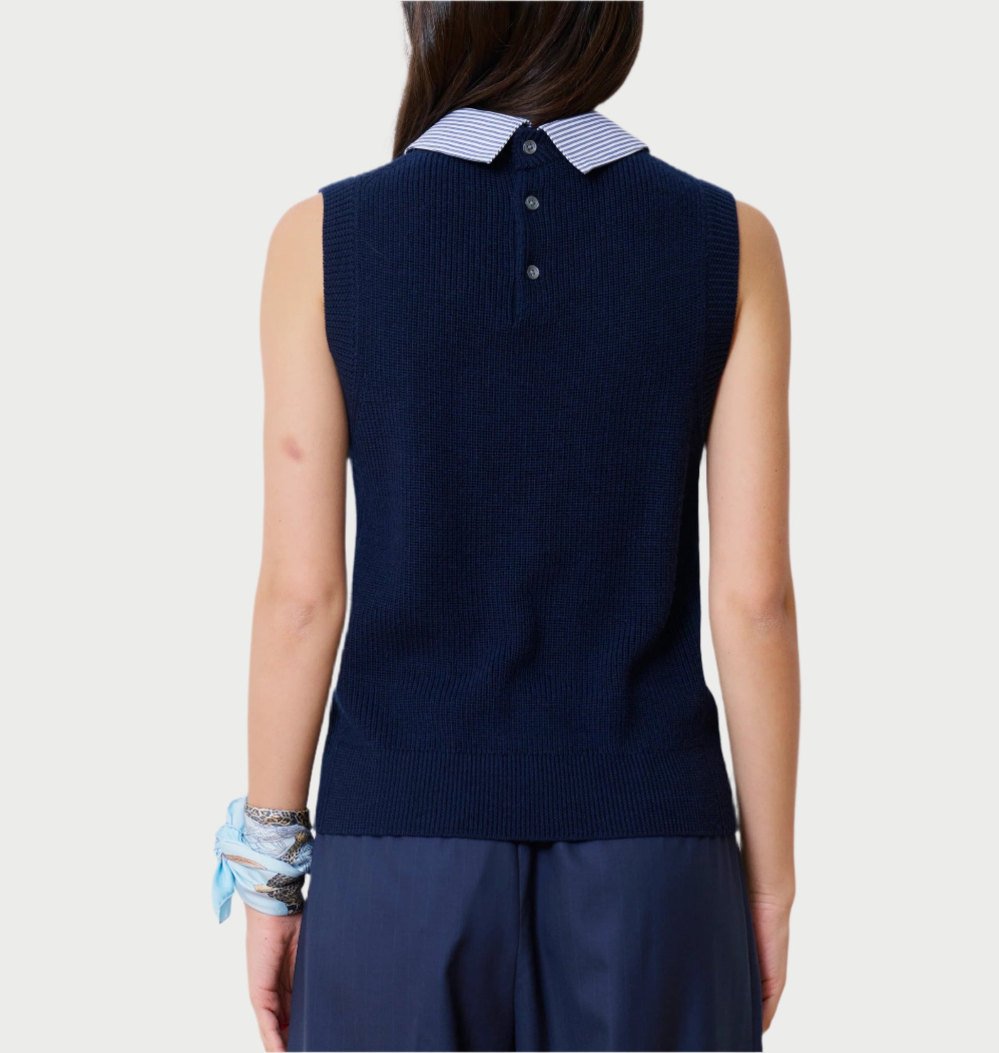 Rear view of a person wearing the School Vest Navy by WE-AR4, featuring a striped collar and button details crafted from luxury deadstock. The person has long dark hair, a blue scarf, and bracelets on their left wrist against a white backdrop.