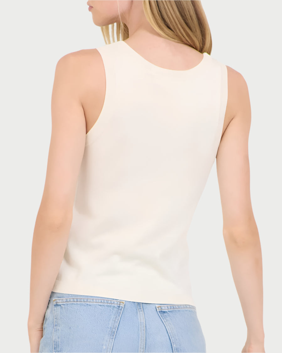 A woman with long blonde hair, wearing a sleeveless white Terra Tank by One Grey Day and light blue jeans, is facing away.