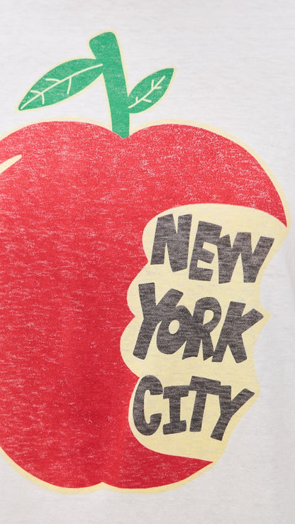 The RE/DONE NYC Big Apple Tee features a red apple with a green stem and leaf, partly eaten to reveal "NEW YORK CITY" in bold black letters—ideal for any vintage New York graphic tee lover.
