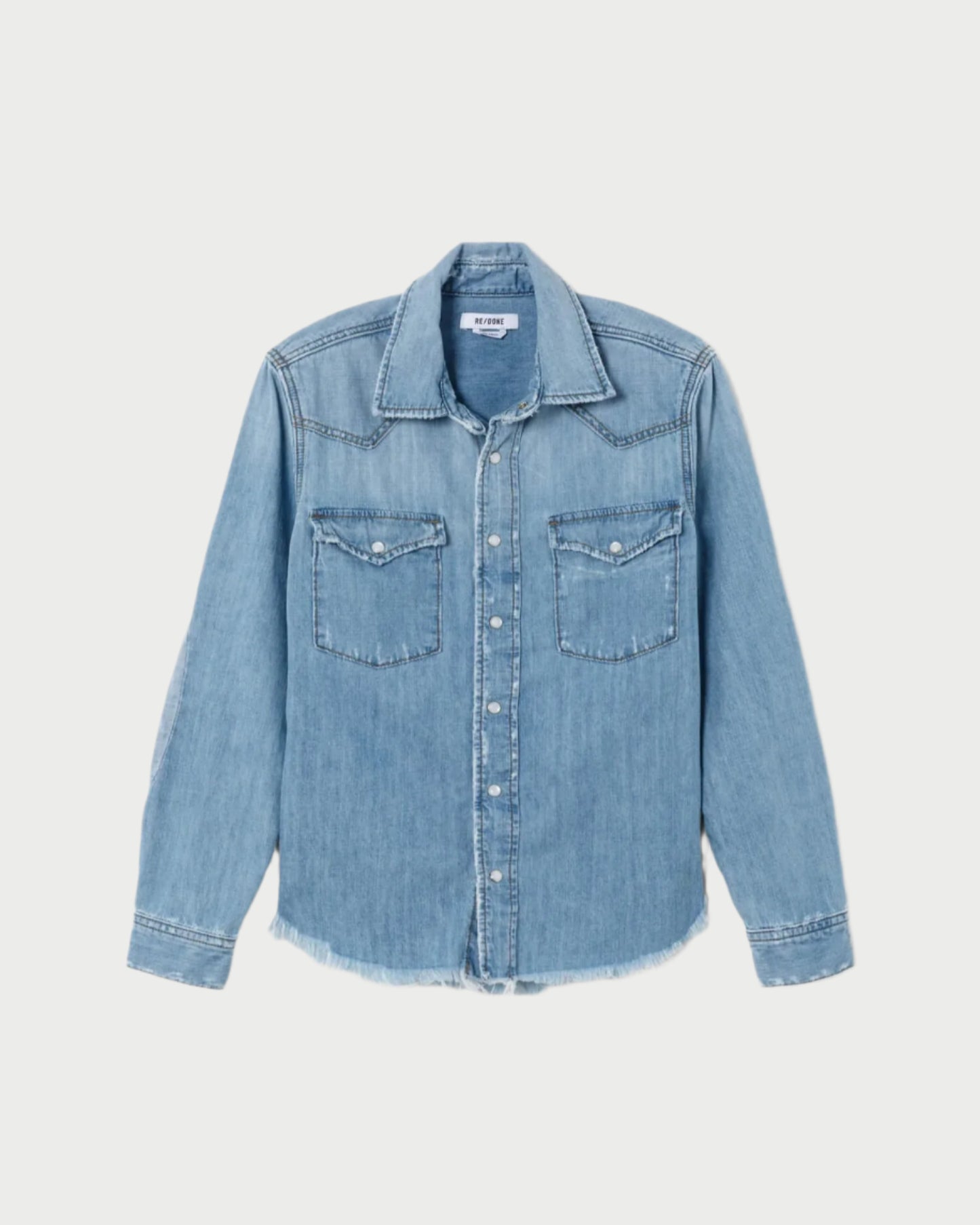 The RE/DONE Western Denim Shirt in light blue features long sleeves, front buttons, and dual chest pockets. Crafted from cotton chambray, it offers a slightly faded look and frayed hem, embodying true rodeo style. It's laid flat against a plain backdrop.