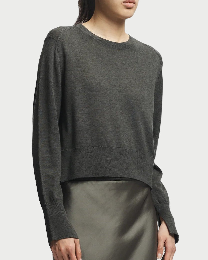 Person wearing a dark green sweater and satin skirt on a light gray background