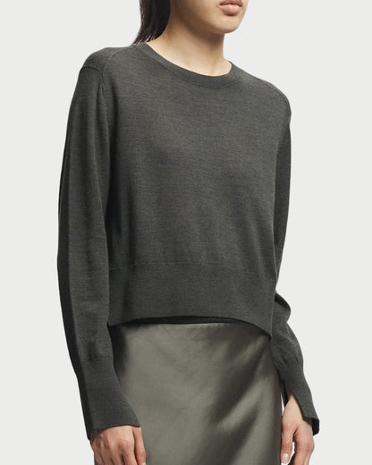 Person wearing a dark green sweater and satin skirt on a light gray background